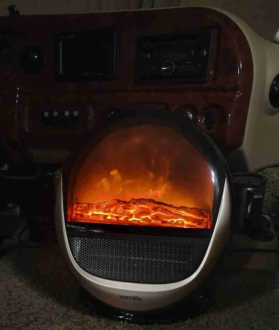 A portable electric heater with a glowing, fiery display placed in front of a vehicle's interior, providing a cozy atmosphere and warmth. small ceramic heater