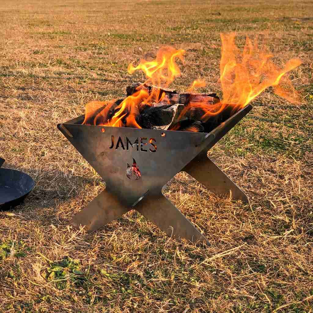Personalized portable fire pits with the name "james" cut into the metal, aflame with bright, dancing flames against a dusky outdoor backdrop.