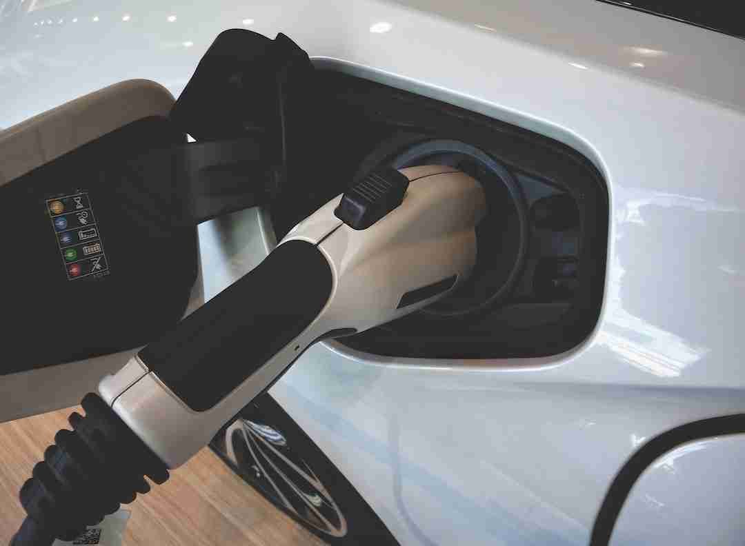 Electric vehicle charging station plug connected to a white car's lithium ion leisure battery charging port. lithium ion leisure batteries