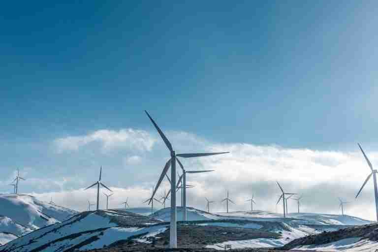 Wind turbines standing tall against a backdrop of snowy hills and a clear blue sky, harnessing the power of the wind to charge lithium leisure batteries.